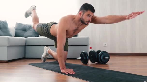 Young man exercising at home. Hold hands and knees on yoga mat and raising one lrg and arm each time during training. Exercising power and strenght - Footage, Video
