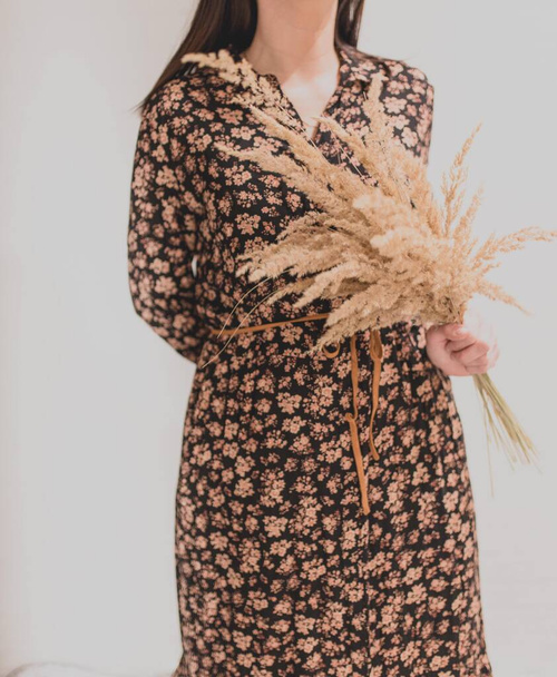 Вертикальный снимок женщины в коричневом цветочном платье с букетом сладкой травы - Фото, изображение