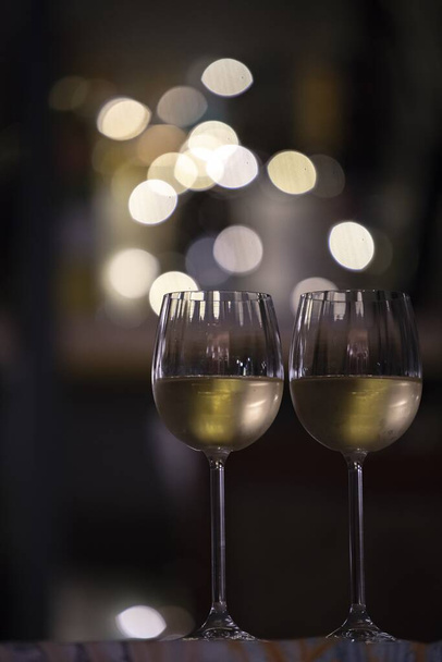 A vertical selective focus shot of two glasses of drink with the blurry lights in the background - 写真・画像