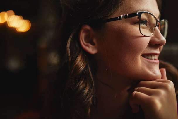 Detailní záběr na usmívající se krásná žena dívá pryč v kavárně a drží ruku na bradě - Fotografie, Obrázek