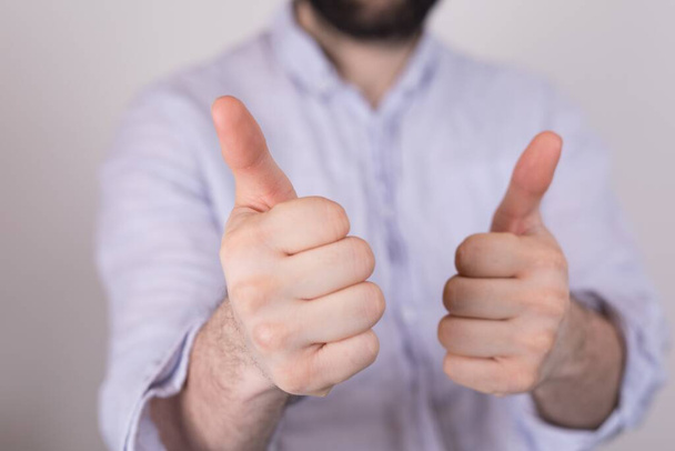 A closeup of a person doing the thumbs-up gesture under the lights on a blurry background - Photo, image