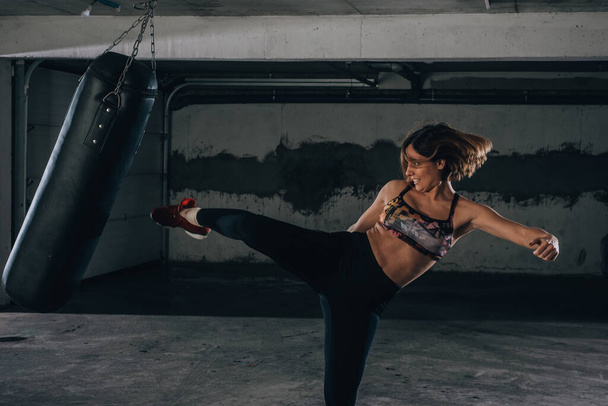 Jonge sportvrouw doet high kick tijdens het boksen oefening in een garage. - Foto, afbeelding