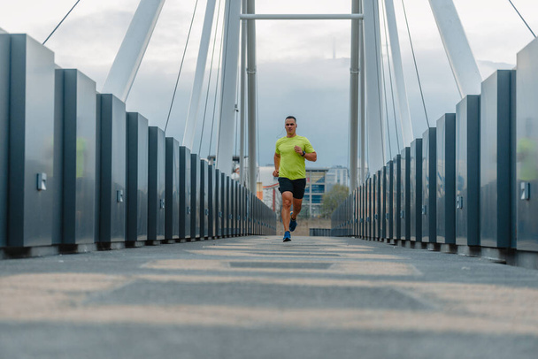 Fit muscular man wearing fitness clothes running across a bridge - Fotó, kép