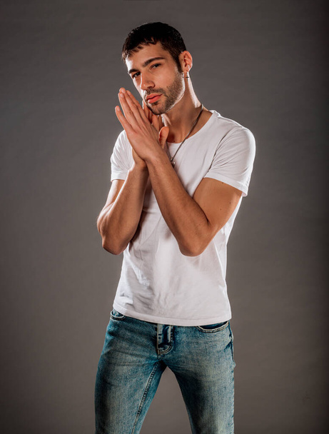 Portrait of a handsome young guy wearing blue denim pants, white t-shirt isolated on grey background - Foto, imagen