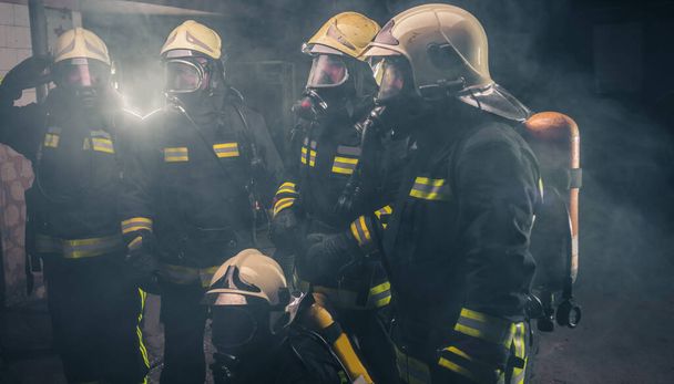 Tűzoltó csapat áll a tűzoltó készülék füstjének közepén a tűzoltóságon belül. - Fotó, kép