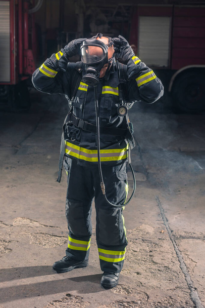 Porträt eines Feuerwehrmannes mit Drehleiter und Helm. Dunkler Hintergrund mit Rauch und blauem Licht. - Foto, Bild
