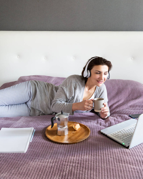 Gri elbiseli genç mutlu kadın evde dinleniyor, kahveyle eğleniyor. Teknoloji aygıtı ile boş zaman, pastel renkler, kopyalama alanı - Fotoğraf, Görsel