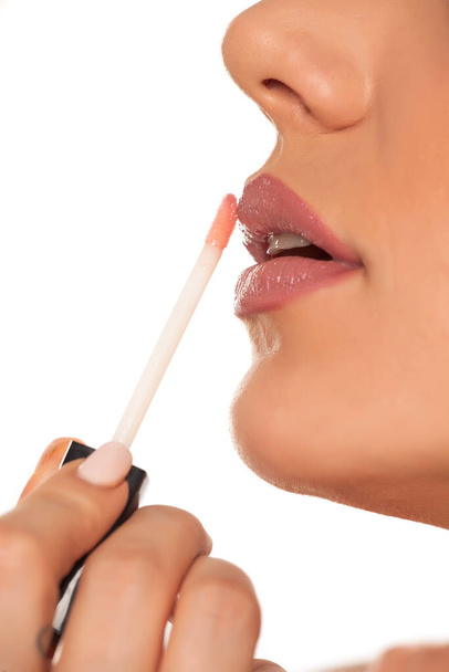 Молодая женщина наносит губный блеск на белый фон
 - Фото, изображение