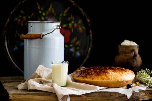 Stillleben mit selbstgebackenem süßen Brot und Milch und Milchkopf in Tonschale und Milchkanne vor schwarzem Hintergrund - Foto, Bild