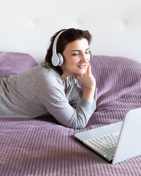 Junge glückliche Frau in Grau entspannt zu Hause und genießt Zeit für sich mit Kaffee. Freizeit mit Technik, Pastellfarben, Kopierraum - Foto, Bild