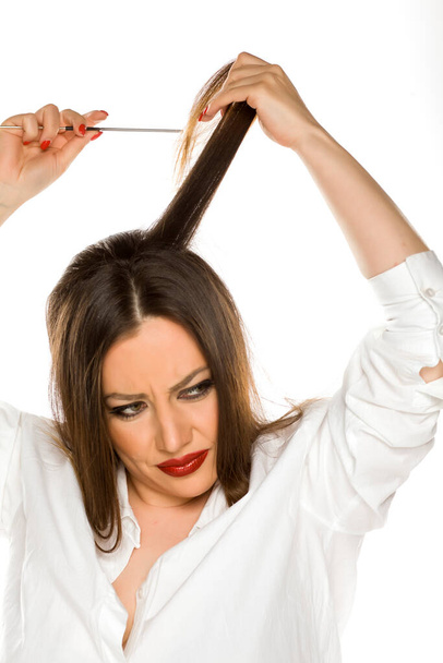 Όμορφη νεαρή νευρική γυναίκα χτενίζει τα μαλλιά της σε λευκό φόντο - Φωτογραφία, εικόνα
