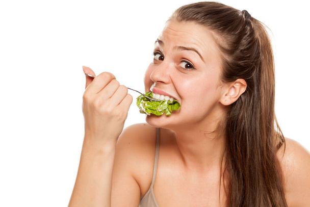joven codiciosa mujer comiendo ensalada de lechuga sobre un fondo blanco
 - Foto, Imagen