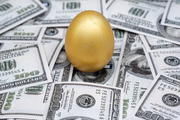 Złote jajko odizolowane na tle banknotu dolara. - Zdjęcie, obraz