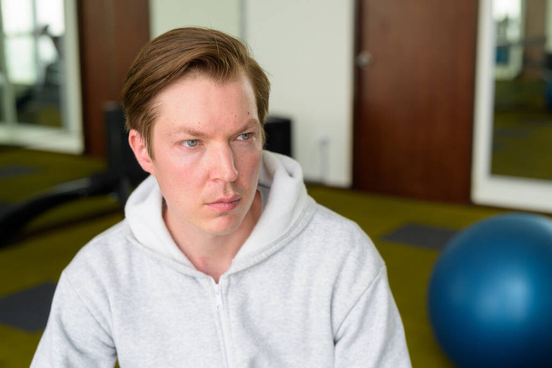 Portrait of young handsome Scandinavian man with hoodie ready for exercising at the gym - Fotó, kép