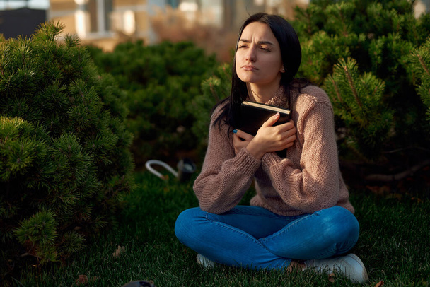 Junge Frau in Freizeitkleidung verbringt Zeit allein im Vorgarten und hält Notizbuch in der Hand - Foto, Bild