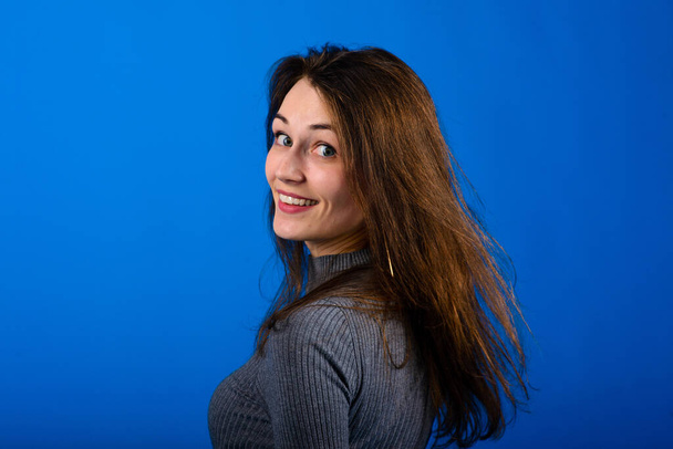 Фото усміхненої, веселої молодої жінки в сірій сукні на синьому фоні. Емоційний портрет
 - Фото, зображення