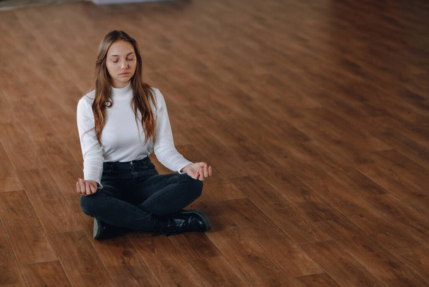 attraktive Business-Stil Mädchen sitzt auf dem Boden in einer Lotusposition. Yoga im Büro, Entspannung bei der Arbeit. Suche nach Harmonie im Geschäftsleben. Yoga und ein harmonischer positiver Geisteszustand. Einfacher Hintergrund. - Foto, Bild