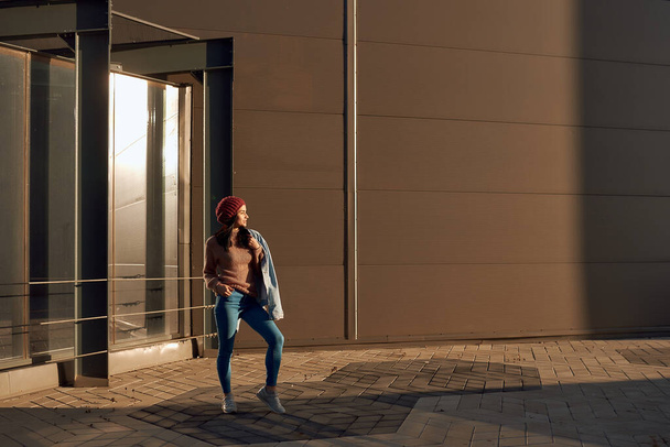 Fiduciosa e bella ragazza bruna in denim elegante in posa all'aperto vicino a un edificio moderno
 - Foto, immagini