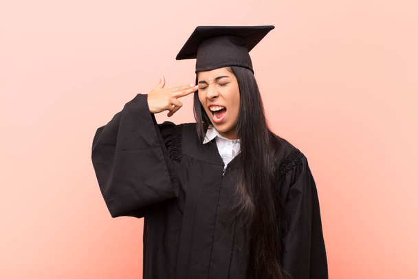 young latin woman student looking unhappy and stressed, suicide gesture making gun sign with hand, pointing to head - Foto, imagen