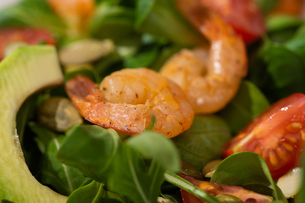 close up view of fresh green salad with pumpkin seeds, cherry tomatoes, shrimps and avocado - Foto, imagen