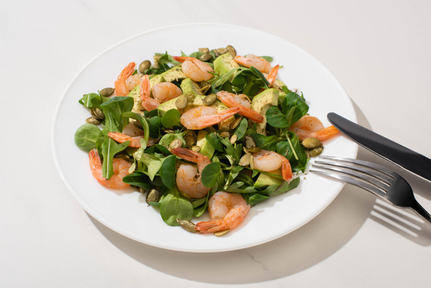 fresh green salad with pumpkin seeds, shrimps and avocado on plate near cutlery on white background - Foto, Bild