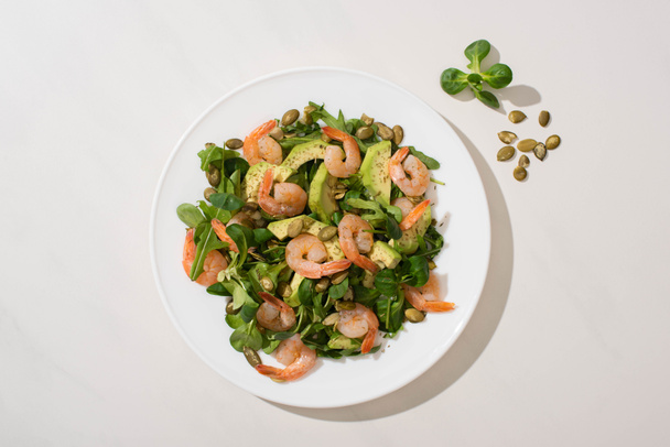 top view of fresh green salad with pumpkin seeds, shrimps and avocado on plate on white background - Fotoğraf, Görsel