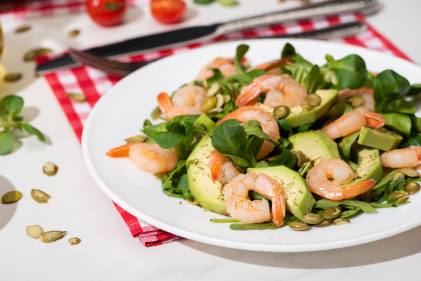 fresh green salad with shrimps and avocado on plate and plaid napkin on white background - Foto, Imagen