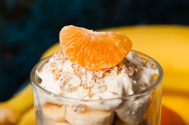 Una rebanada de mandarina macro encima de un postre. Yogur con plátano, mandarina y avena
 - Foto, imagen