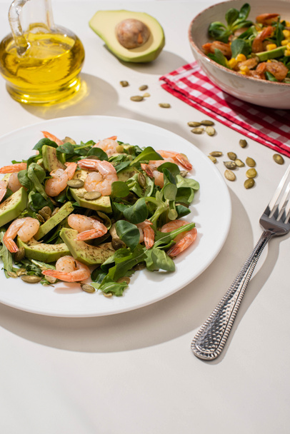 selective focus of fresh green salad with shrimps and avocado on plates near fork and oil - Foto, Imagen