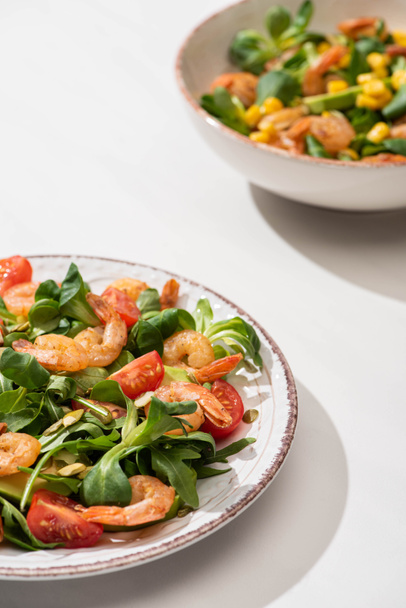 selective focus of fresh green salad with shrimps and avocado on plates on white background - Foto, Bild