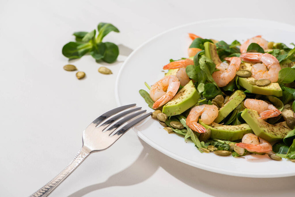 selective focus of fresh green salad with shrimps and avocado on plate near fork on white background - Foto, immagini