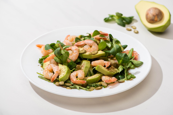 Enfoque selectivo de ensalada verde fresca con camarones y aguacate en plato sobre fondo blanco
 - Foto, Imagen