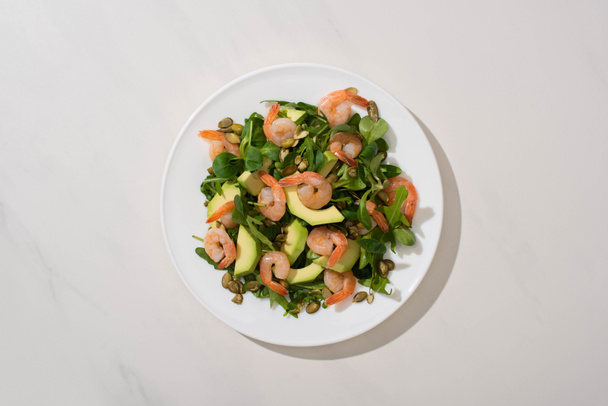 top view of fresh green salad with pumpkin seeds, shrimps and avocado on plate on white background - Photo, image