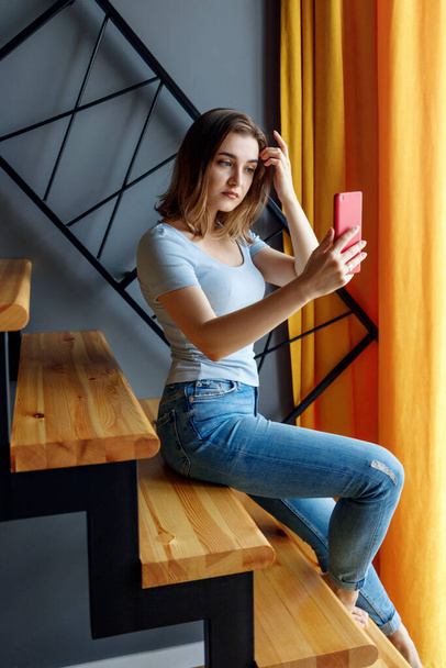 Young woman looks in smartphone and makes selfie on the staircase. - Photo, Image