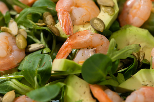 Nahaufnahme von frischem grünen Salat mit Kürbiskernen, Garnelen und Avocado - Foto, Bild