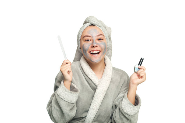 Un'adolescente con una maschera cosmetica sul viso fa una manicure. Maschera viso scrub. Il concetto di salute e bellezza. - Foto, immagini