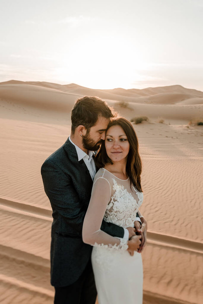 Una pareja en sus vestidos de novia en el desierto se divierten mientras posan en el desierto. Concepto de boda
 - Foto, imagen