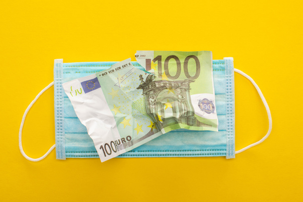 Draufsicht auf zerrissene Euro-Banknote und medizinische Maske auf gelbem Hintergrund - Foto, Bild