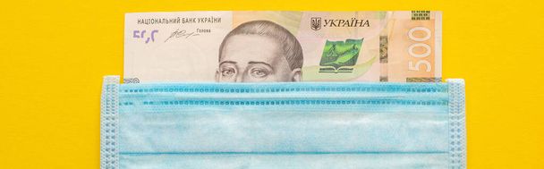 vista superior del billete de Ucrania y máscara médica sobre fondo amarillo, plano panorámico
 - Foto, Imagen