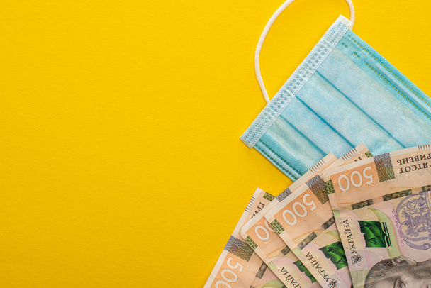 Sarı arka planda Ukrayna banknotlarının ve tıbbi maskenin üst görüntüsü - Fotoğraf, Görsel