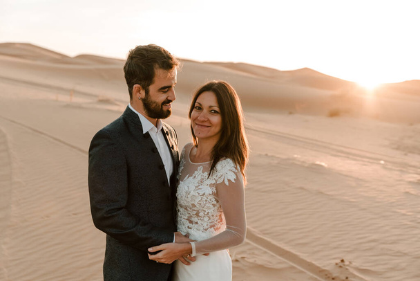 Una pareja en sus vestidos de novia en el desierto se divierten mientras posan en el desierto. Concepto de boda
 - Foto, Imagen