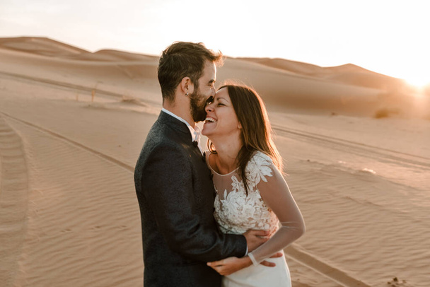 Ein Paar im Brautkleid in der Wüste amüsiert sich, während es in der Wüste posiert. Hochzeitskonzept - Foto, Bild