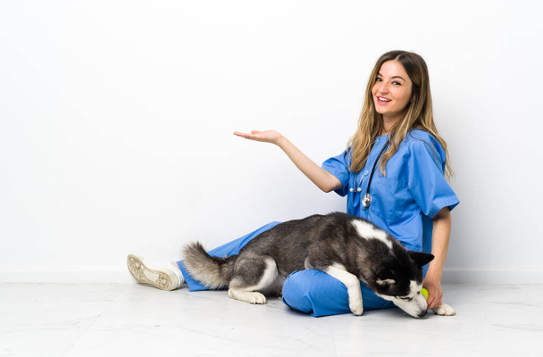 Veterinární lékař se Sibiřský Husky pes sedí na podlaze natahuje ruce na stranu pro pozvání přijít - Fotografie, Obrázek