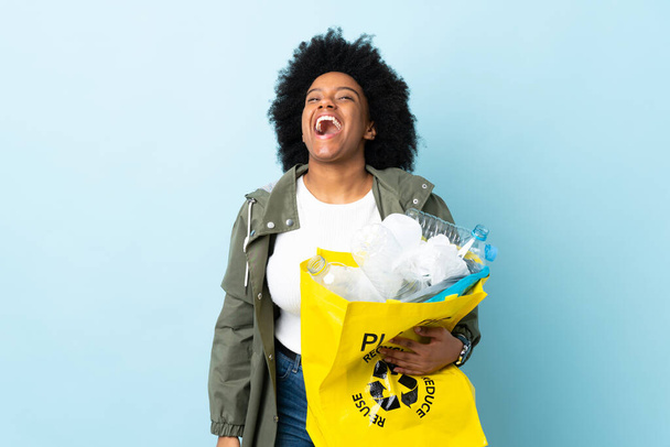 Νεαρή Αφρο-Αμερικανίδα που κρατάει μια τσάντα ανακύκλωσης απομονωμένη σε πολύχρωμο φόντο γελώντας - Φωτογραφία, εικόνα