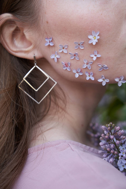 Part of the girl's face, lilac petals on her cheek                                 - Photo, image