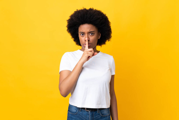 Młoda Afroamerykanka odizolowana na żółtym tle wykazująca znak milczenia wkładająca palec do ust - Zdjęcie, obraz
