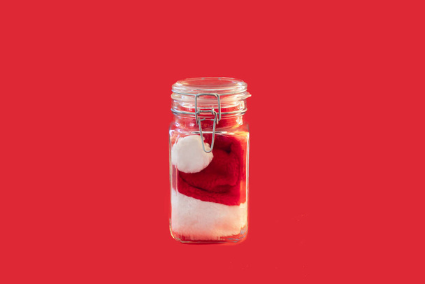 Chapeau de Père Noël dans un récipient en verre sur un fond rouge
 - Photo, image