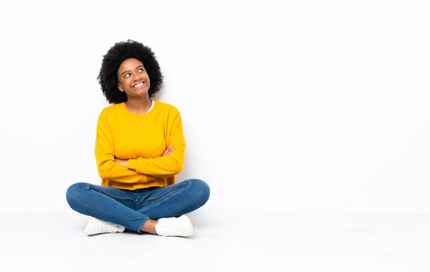 Mladá africká americká žena sedí na podlaze a dívá se nahoru s úsměvem - Fotografie, Obrázek