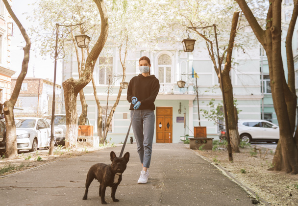 mujer en máscara médica y guantes de látex caminando con adorable bulldog francés en la calle
  - Foto, imagen