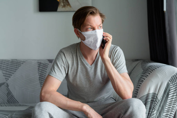 Portrait of young man with mask for protection from corona virus outbreak staying at home during quarantine for covid-19 - Фото, изображение